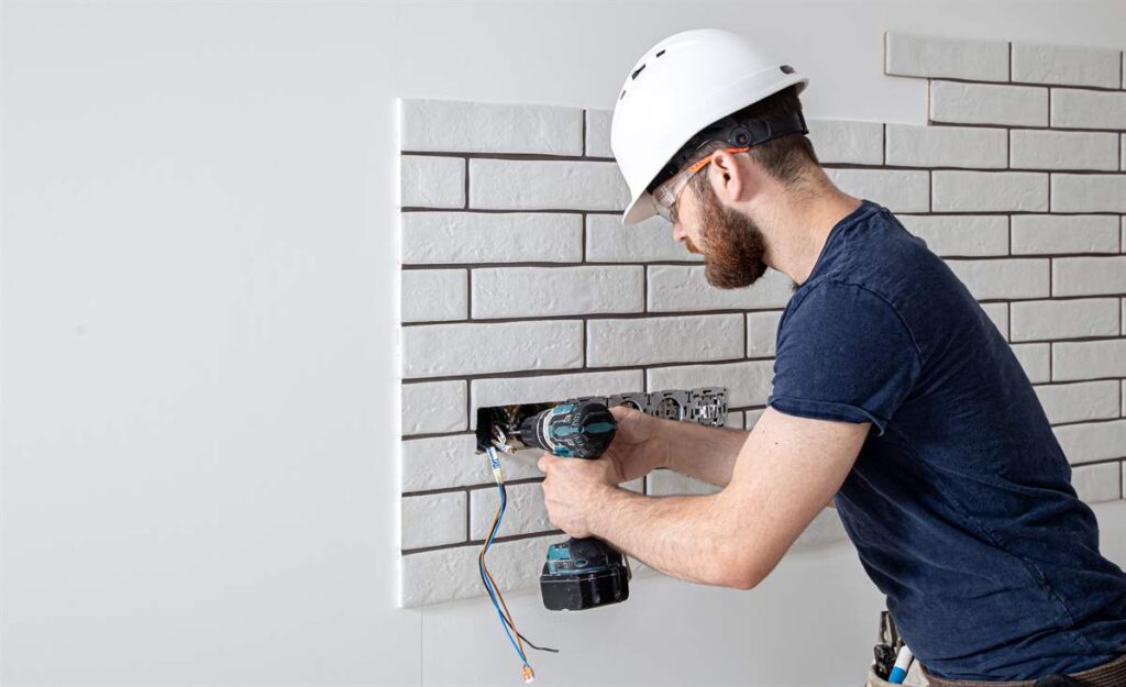 Electrician Construction worker using a drill for socket installation at home